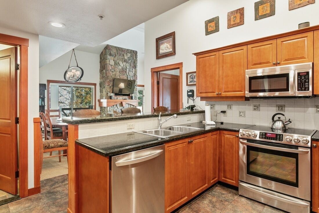 A kitchen with wooden cabinets, stainless steel appliances, a stone accent wall, and a dining area with a view.