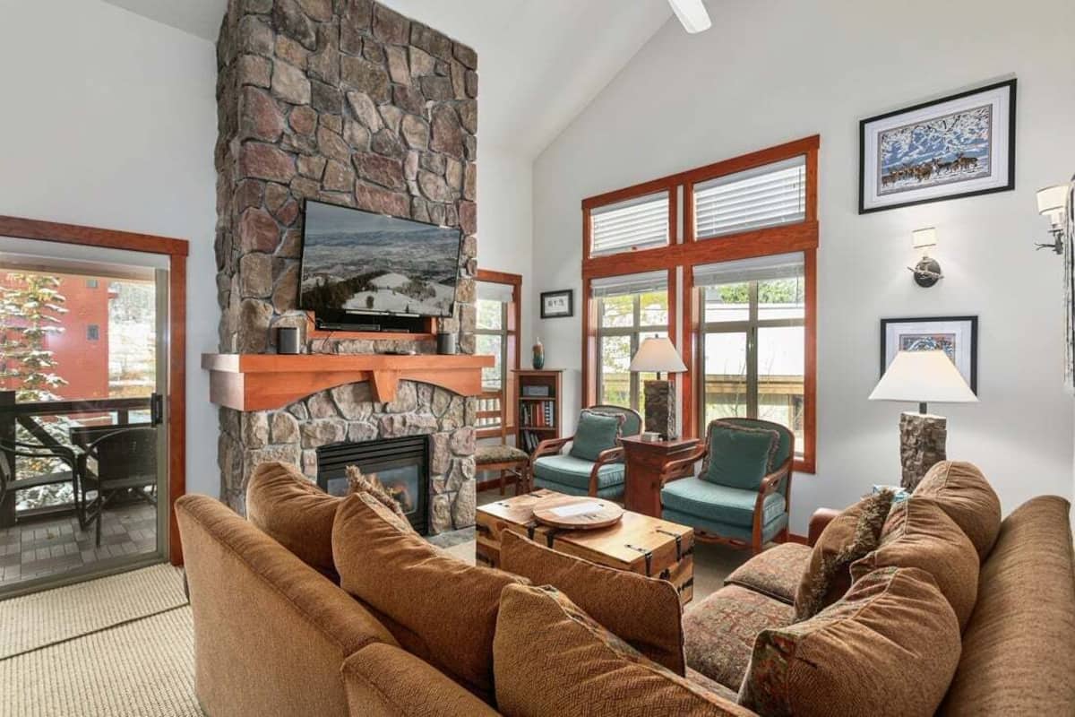 A cozy living room with a stone fireplace, comfortable seating, and large windows.