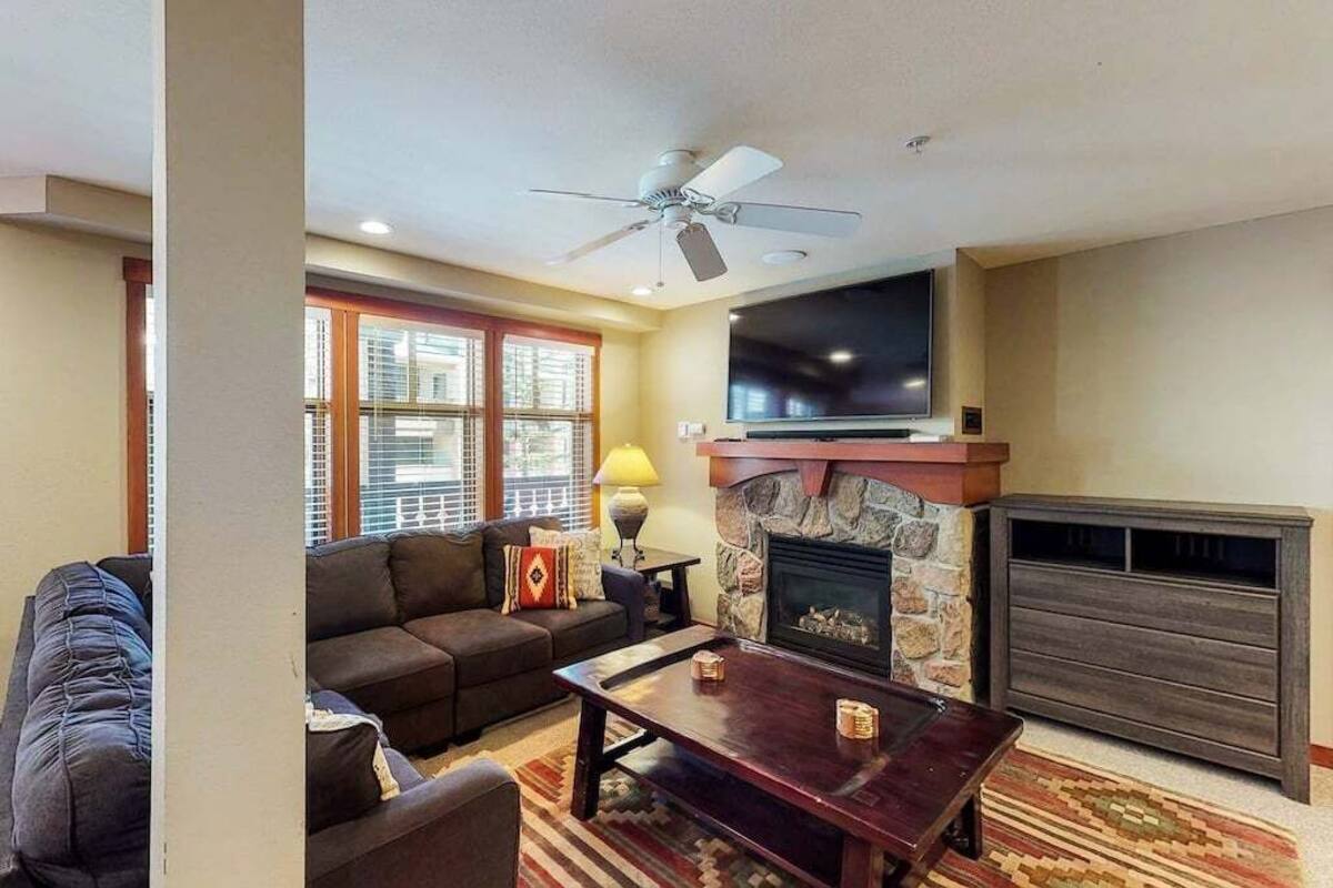 A living room with a sofa, a coffee table, a fireplace, a television, and a ceiling fan.
