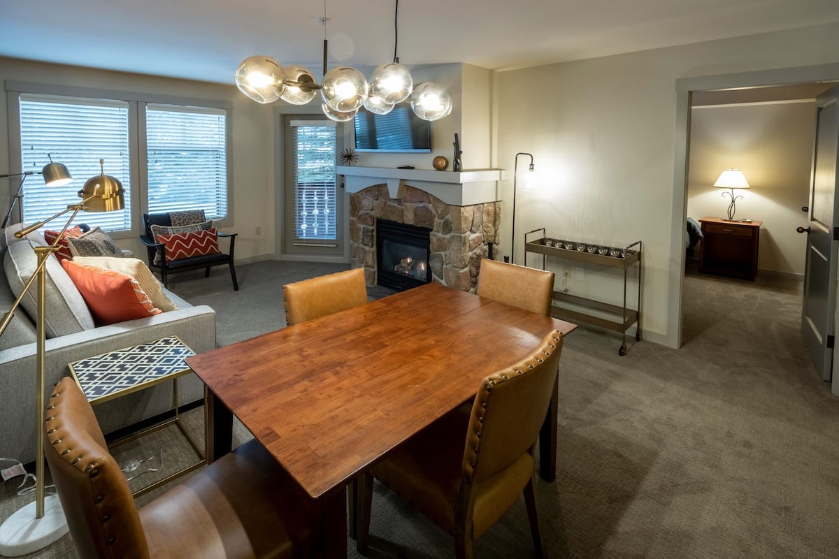A dining area with a wooden table and chairs, a stone fireplace, and a television above it.