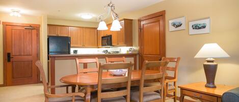 A compact kitchen with wooden cabinets, a refrigerator, and a dining area with a table and chairs.