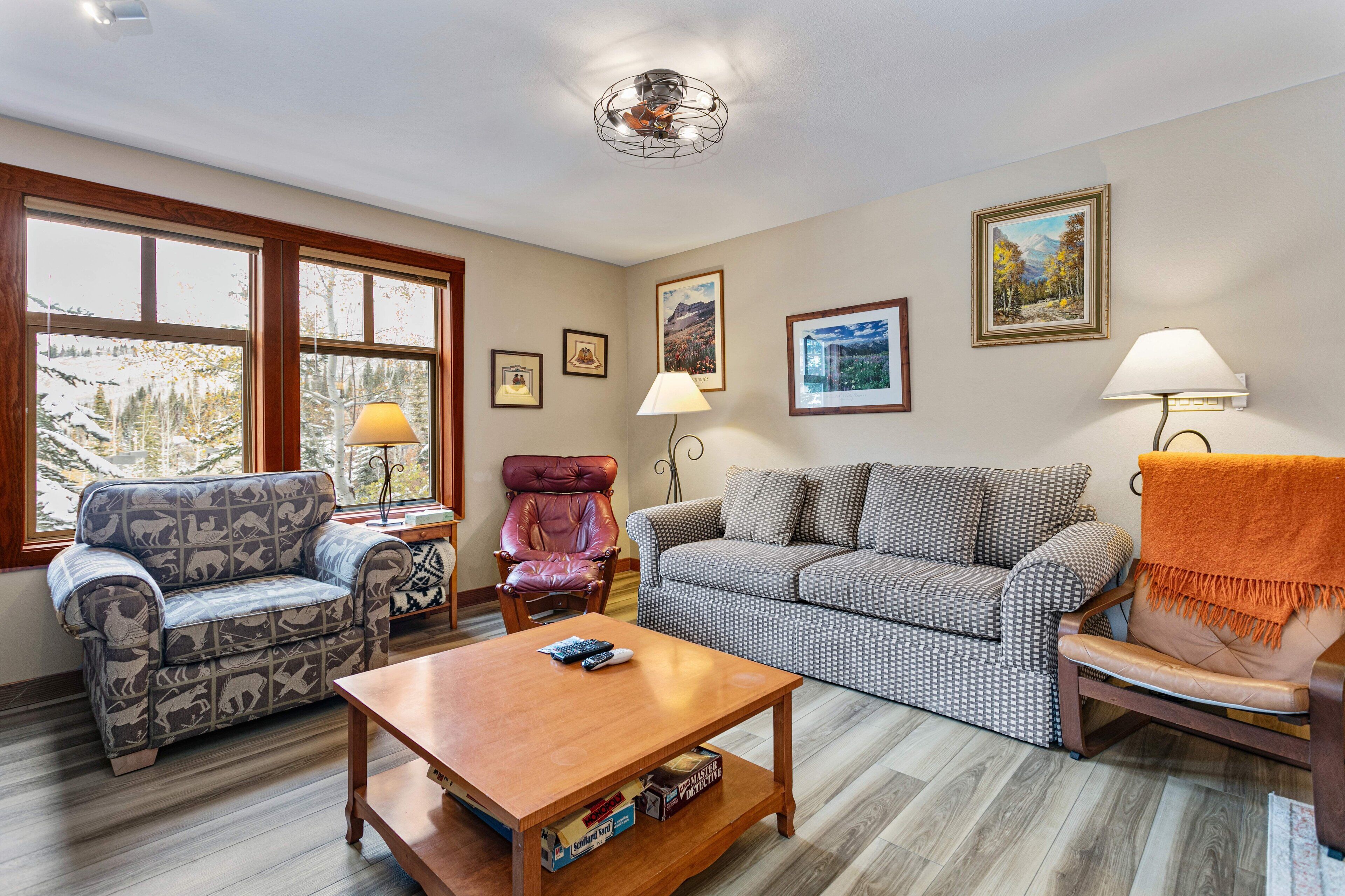 Un salon chaleureux avec un canapé à motifs, un fauteuil en cuir, une table basse en bois et une cheminée.