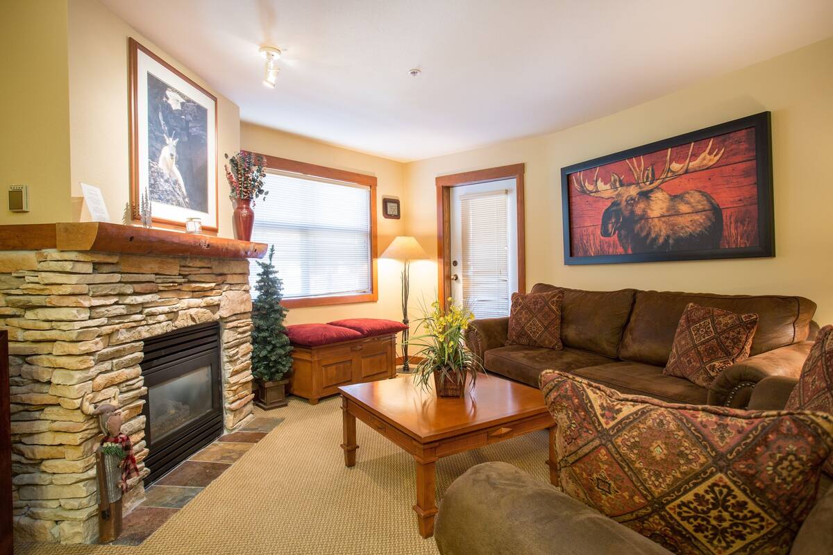 A cozy living room with a stone fireplace, a brown leather sofa, and a large moose painting on the wall.