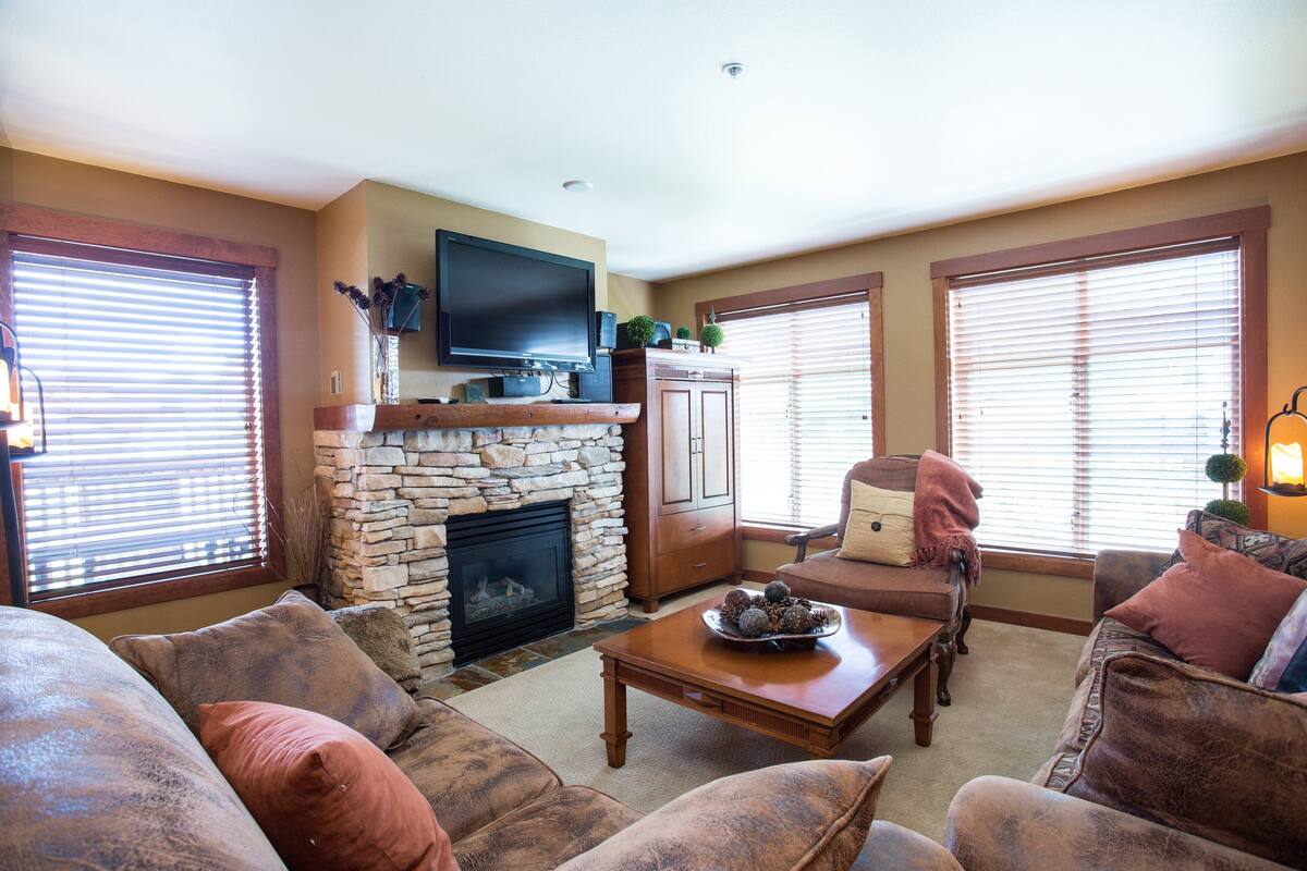 A living room with a stone fireplace, a flat-screen TV mounted above it, and a comfortable seating area with sofas and a coffee table.