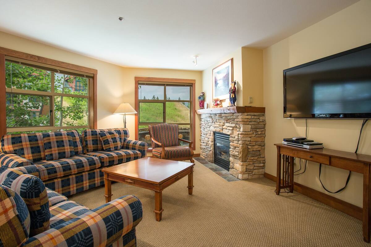 A living room with a sofa, armchair, fireplace, television, and a stone wall.