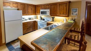 A kitchen with wooden cabinets, a stainless steel sink, a microwave, and a stove. - Powderhorn Lodge Cozy Condos - Solitude UT (Solitude)