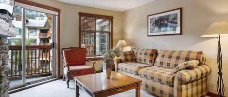 A living room with a sofa, armchair, coffee table, and a large window with a view of a balcony.