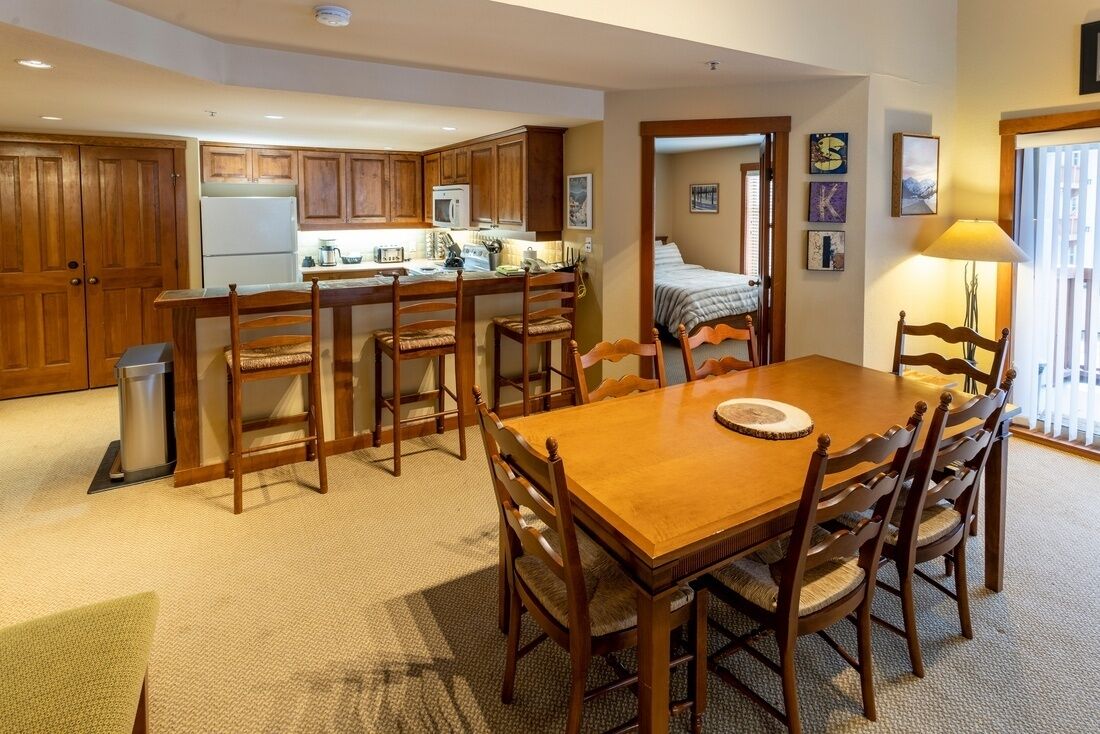 Una cocina acogedora con armarios de madera, una mesa de comedor con sillas y una pequeña isla con fregadero y microondas.