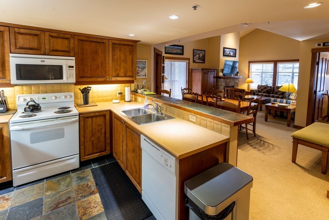 A kitchen with wooden cabinets, a microwave, stove, and dishwasher. There is a dining area with a table and chairs.