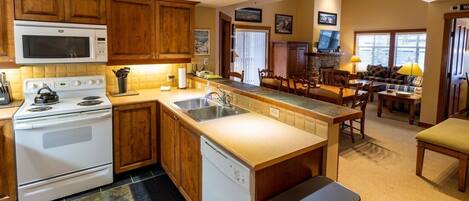 A kitchen with wooden cabinets, a microwave, stove, and dishwasher. There is a dining area with a table and chairs.