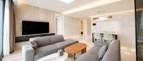 Una sala de estar moderna con un televisor de pantalla plana grande, sofás grises, una mesa de centro de madera y un comedor con sillas y una mesa.