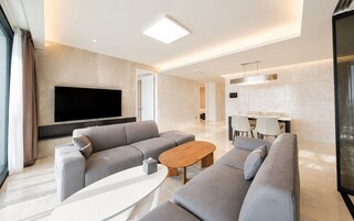 Una sala de estar moderna con un televisor de pantalla plana grande, sofás grises, una mesa de centro de madera y un comedor con sillas y una mesa.