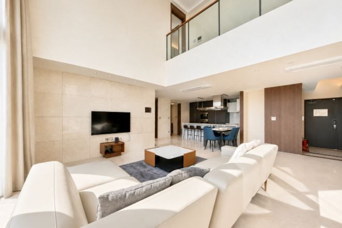 A modern living room with a flat-screen TV, a sofa, a coffee table, and a dining area in the background.