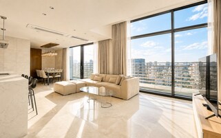 Una sala de estar moderna con un sofá seccional, un comedor y un amplio ventanal con vista a la ciudad.