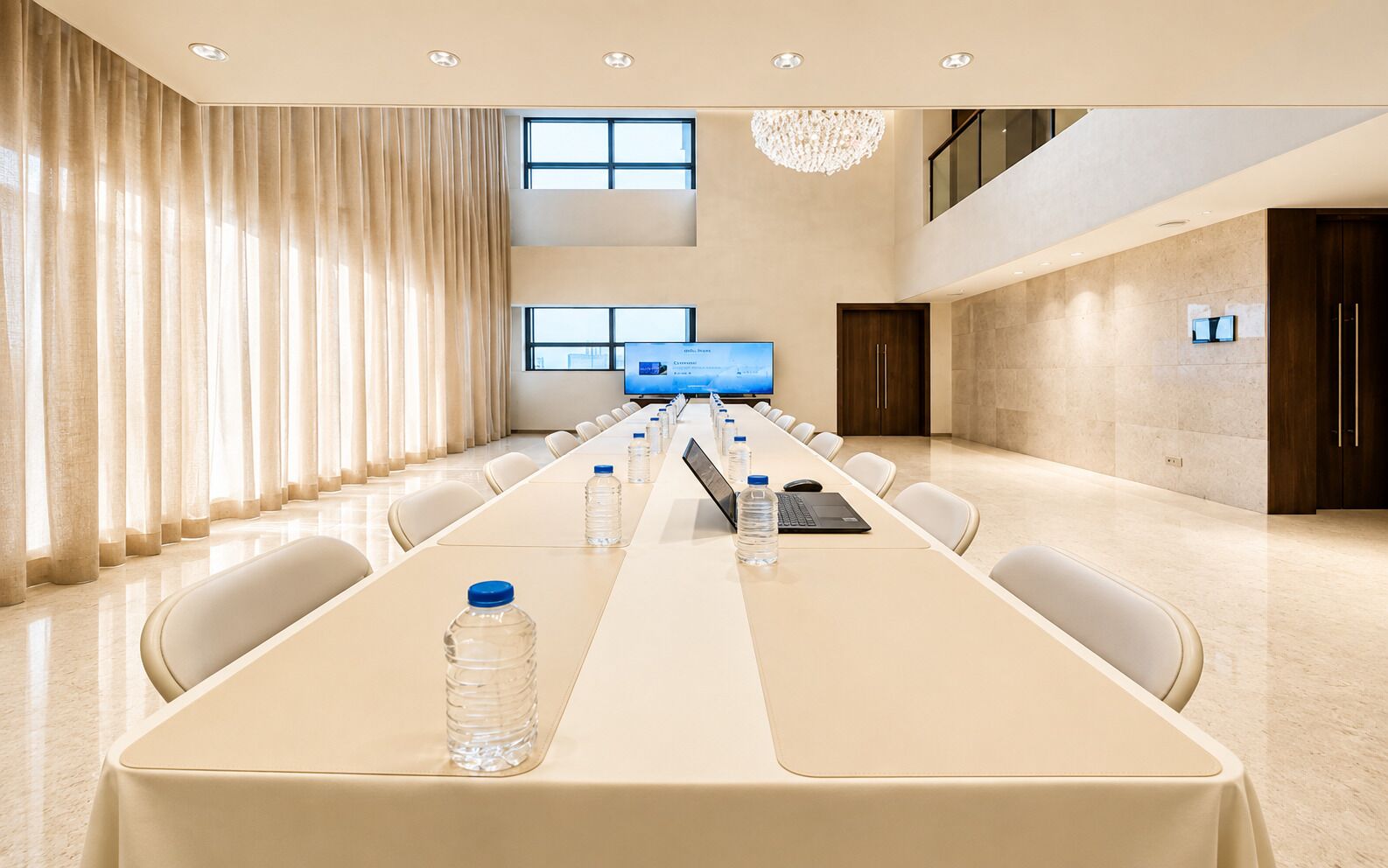 A conference room with a long table, chairs, water bottles, a laptop, and a television screen.