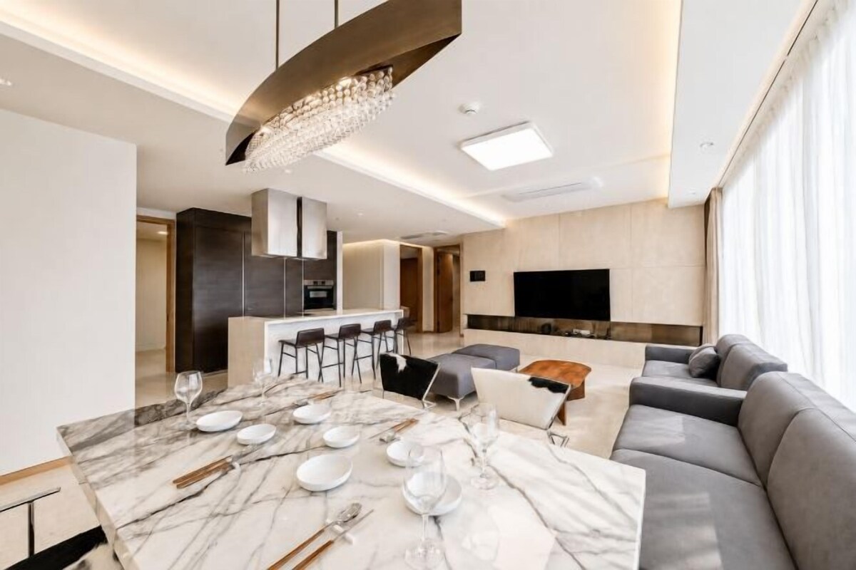 Una sala de estar moderna con una mesa de comedor de mármol dispuesta para cuatro personas, un sofá gris y un televisor en la pared.