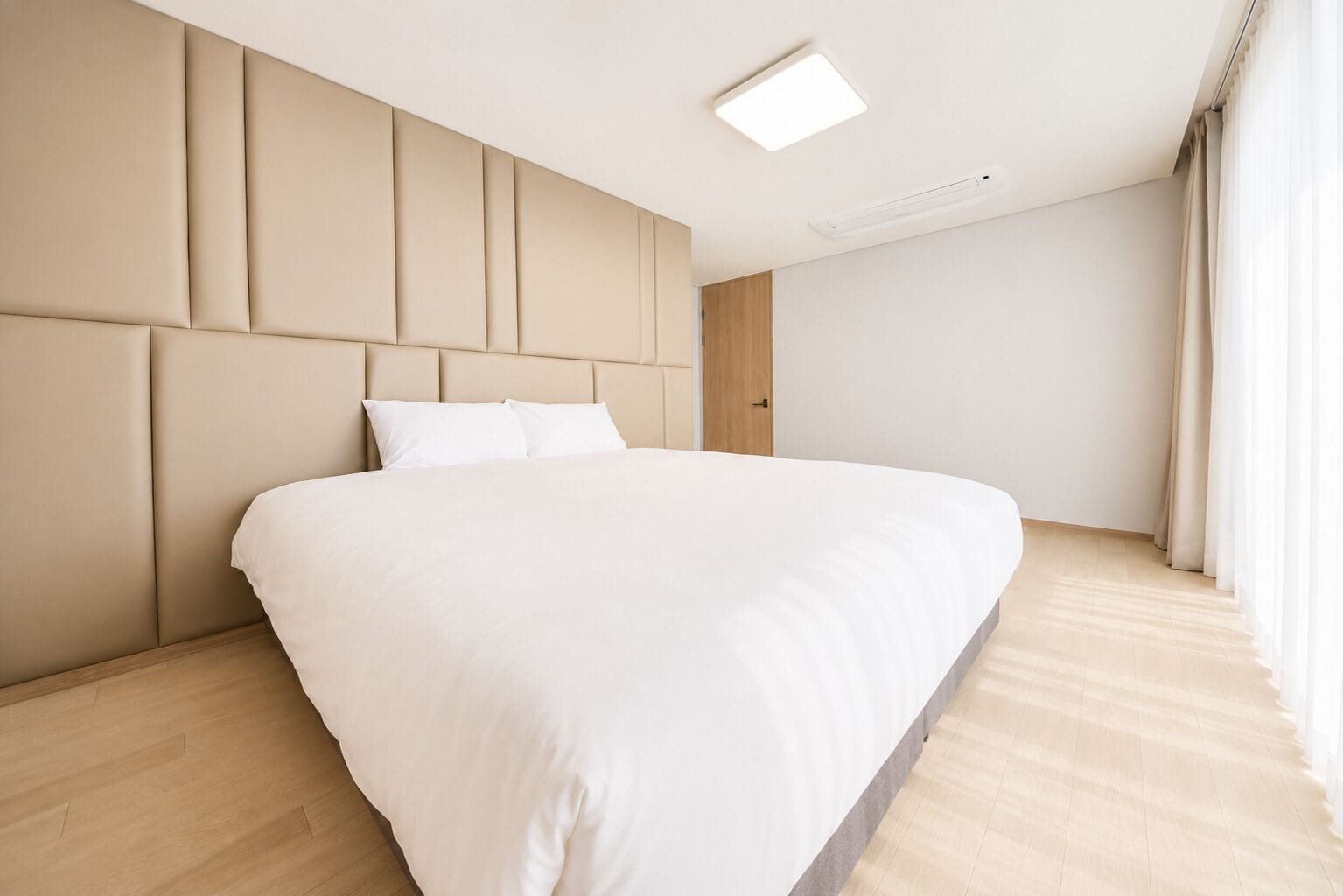 A modern bedroom with a large bed, a headboard with vertical panels, a ceiling light, and a door.