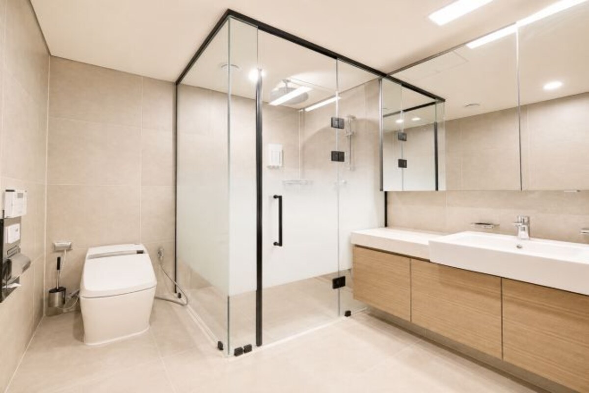 A modern bathroom with a glass shower enclosure, a white toilet, and a wooden vanity with a mirror.