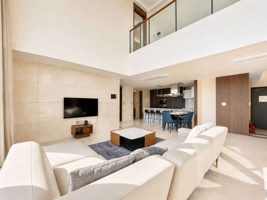 Una sala de estar moderna con una televisión de pantalla plana, una mesa de centro y un sofá. Hay un comedor con sillas y una cocina al fondo.