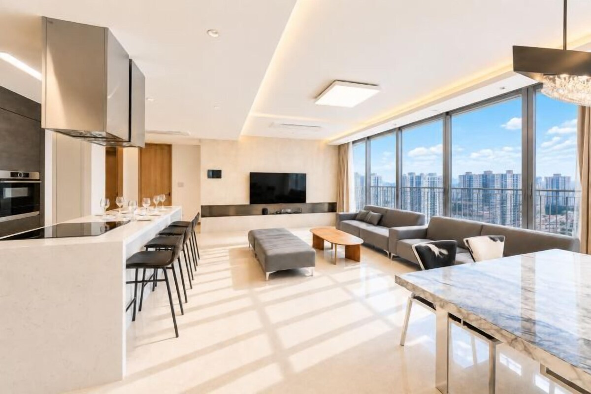 A modern apartment with a kitchen, dining area, and living room, featuring a large window with a city view.