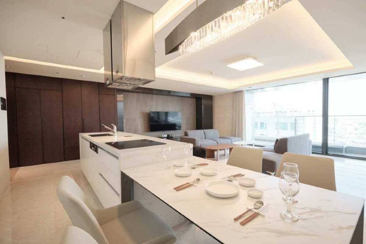 Une cuisine moderne dotée d’un îlot central, un coin repas avec une table en marbre et un espace de vie avec une grande fenêtre.
