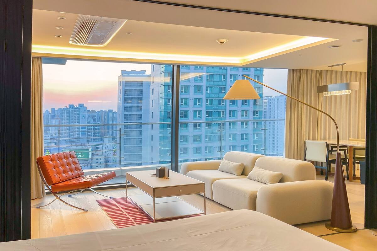 Une chambre d’hôtel moderne dotée d’une grande fenêtre donnant sur la ville, d’un canapé, d’un fauteuil et d’un bureau.