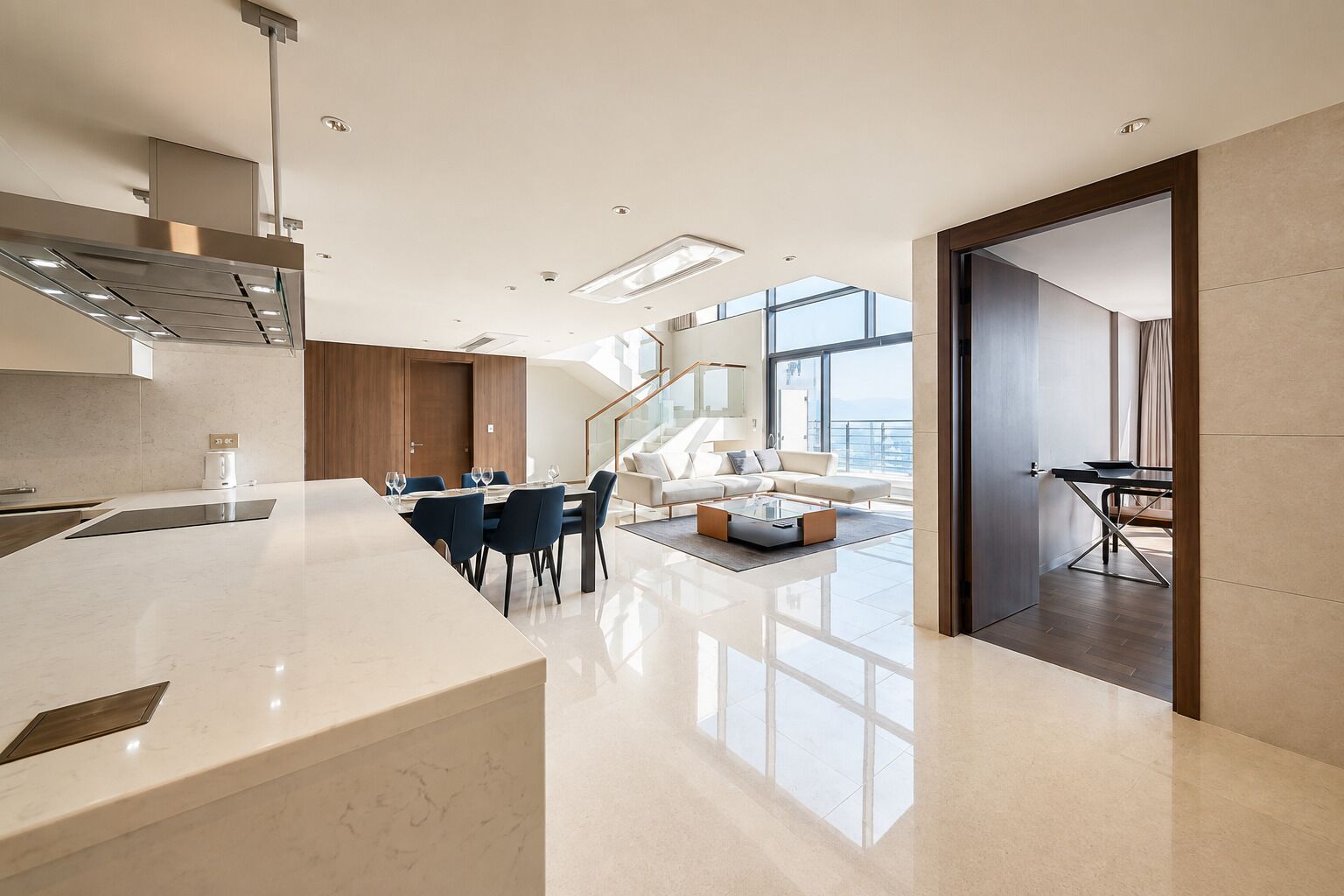 Cocina moderna con encimera de mármol, comedor con mesa y sillas, y sala de estar con sofá y mesa de centro.