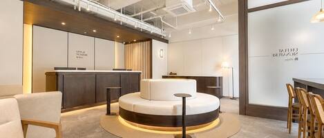 Un área de recepción moderna con una disposición circular de asientos, una mesa de recepción y una pared con señalización.