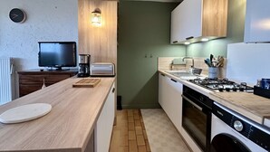 Een kleine keuken met een houten aanrecht, een gasfornuis, een wasmachine en een koffiezetapparaat.
