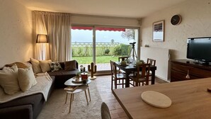 Un salon comprenant un canapé, une table à manger, des chaises, un téléviseur et une fenêtre avec des rideaux.