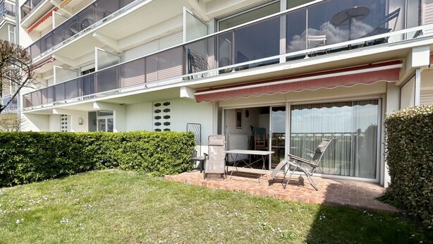 Un immeuble résidentiel à plusieurs étages doté de balcons, d’un patio aménagé avec du mobilier d’extérieur et d’un jardin bien entretenu.