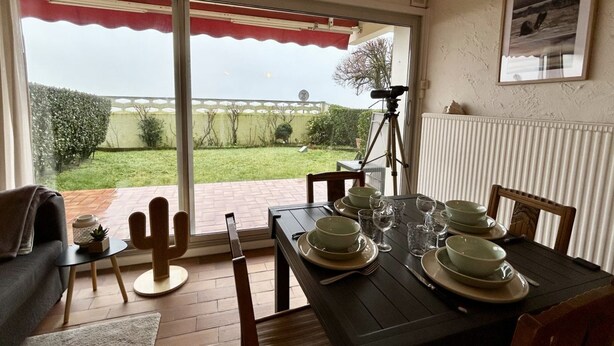 Een eethoek met een tafel voor vier personen, een cactusdecoratie en uitzicht op een tuin door een schuifdeur.