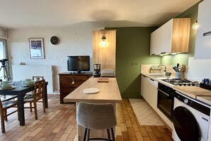 A compact kitchen with a dining area, a television, and a washing machine. - Jardin sur Baie, 4-person ground-floor apartment with sea view (Le Crotoy)