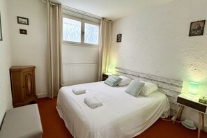 A neatly made bed with pillows and a bedside table with a lamp. - Jardin sur Baie, 4-person ground-floor apartment with sea view (Le Crotoy)