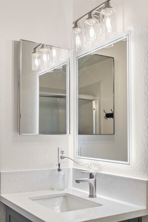 Une salle de bain avec un lavabo blanc, un miroir et un luminaire placé au-dessus du miroir.