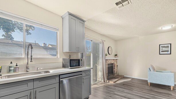 A modern kitchen with grey cabinets, a dishwasher, and a microwave. There's a large window with a view of the outside. - Peaceful and Quiet 4 Br house with Garage (Sacramento)