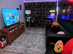 Een woonkamer met een tv waarop streamingdiensten, een spelconsole en arcade games worden getoond.
