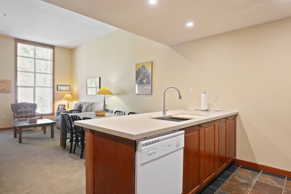 A compact kitchen with a dishwasher, a dining area with a table and chairs, and a window providing natural light.