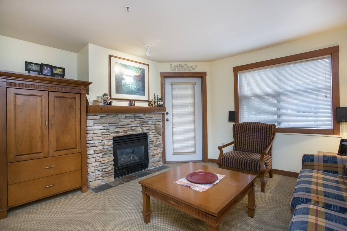 A living room with a stone fireplace, wooden furniture, a plaid sofa, and a door with a window.