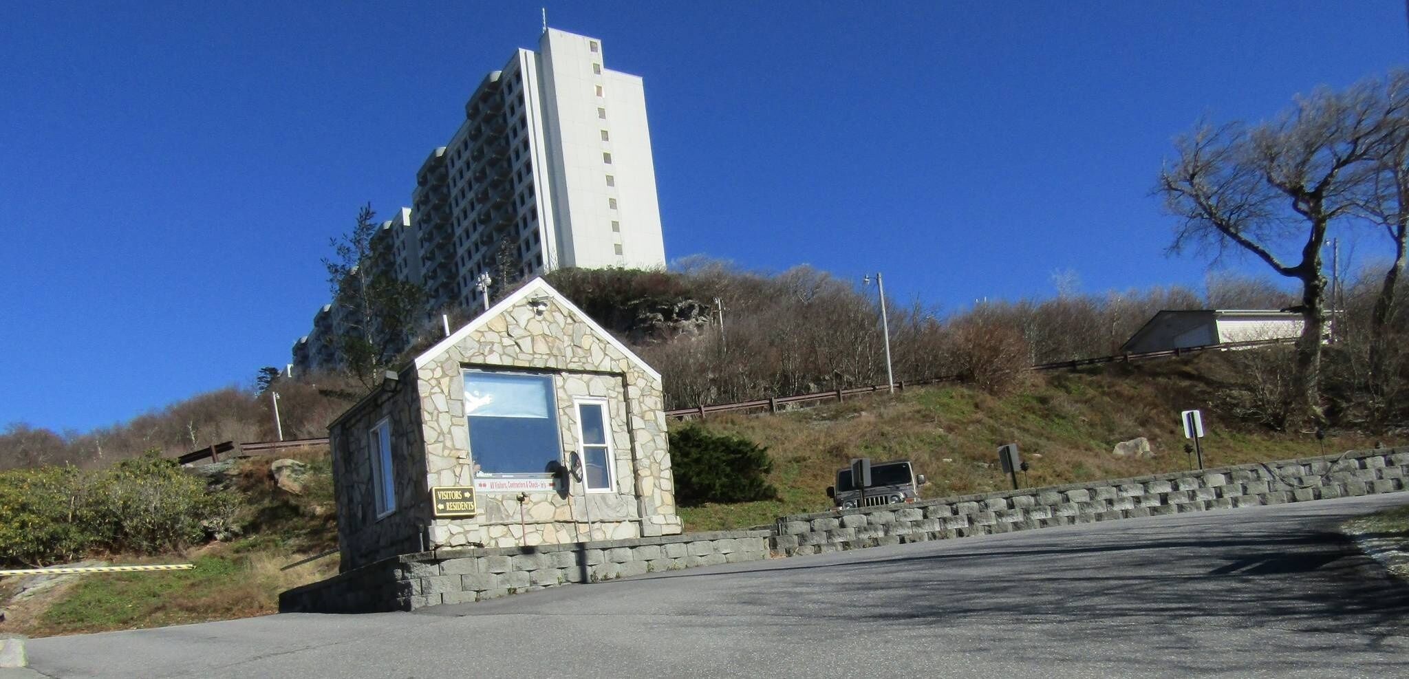 A stone building with a sign for visitors and residents, located near a road with a guardrail and a tall building in the background.