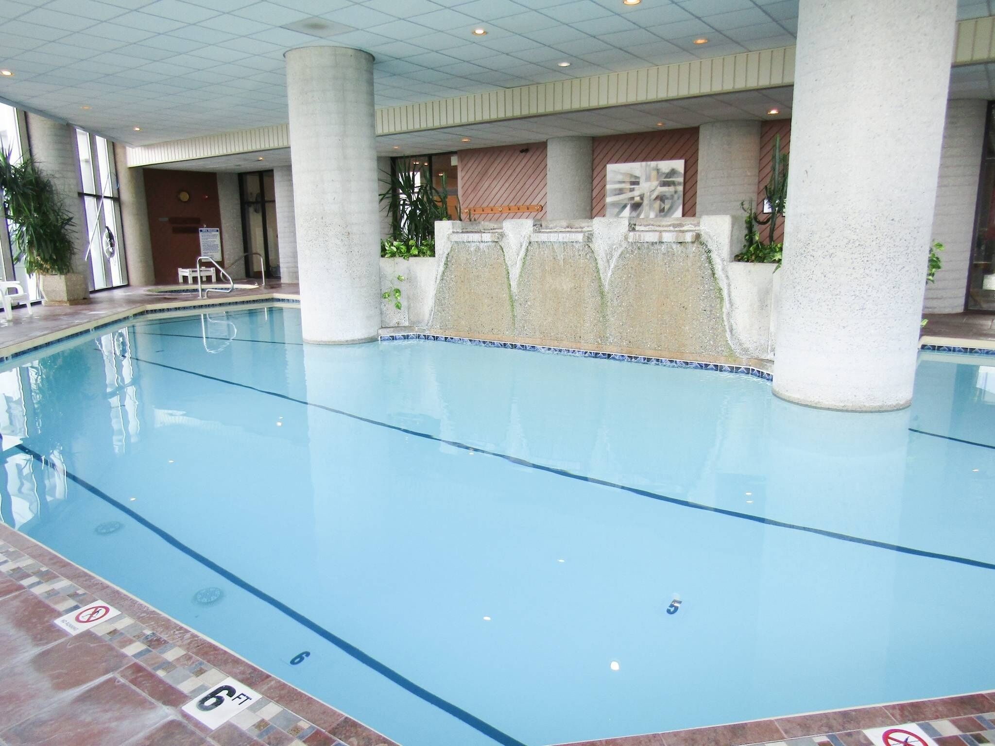 An indoor swimming pool with clear water, surrounded by columns and a tiled floor.