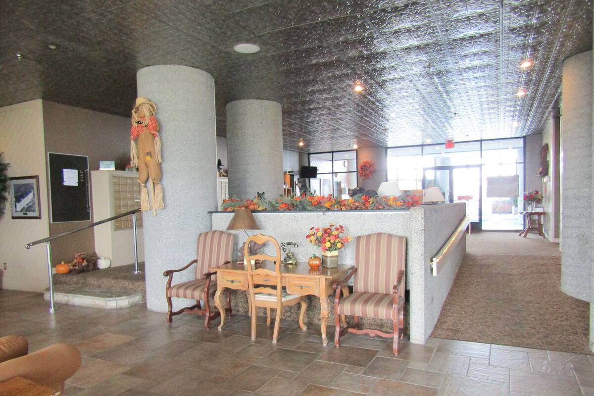 A lobby with a reception desk, striped chairs, a wooden table, and a decorative plant.