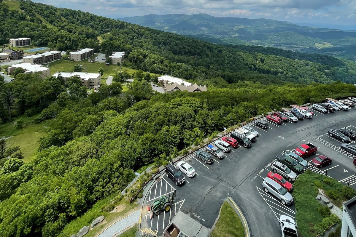 A parking lot with multiple vehicles, surrounded by lush greenery and hills in the background.