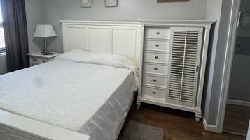A bedroom with a bed, a dresser, a nightstand, a ceiling fan, and a door.
