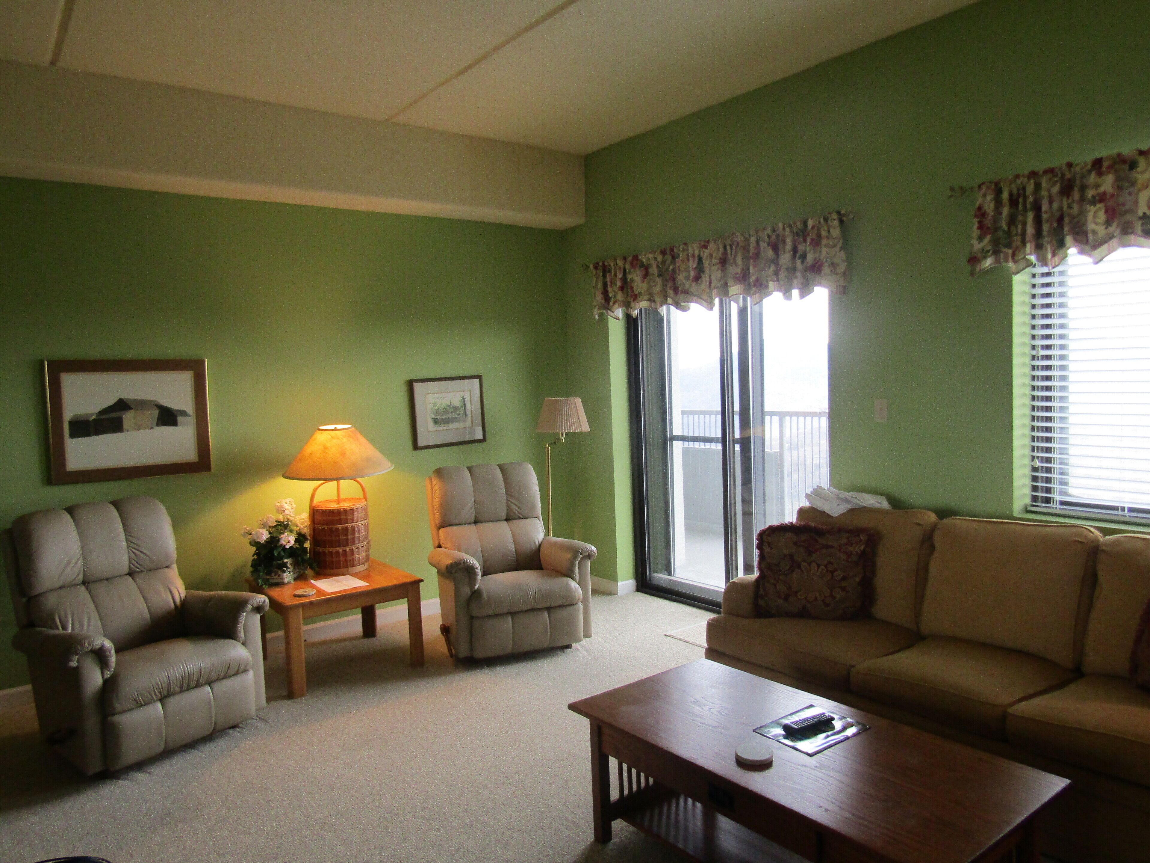 A living room with green walls, two armchairs, a sofa, a coffee table, and a lamp.