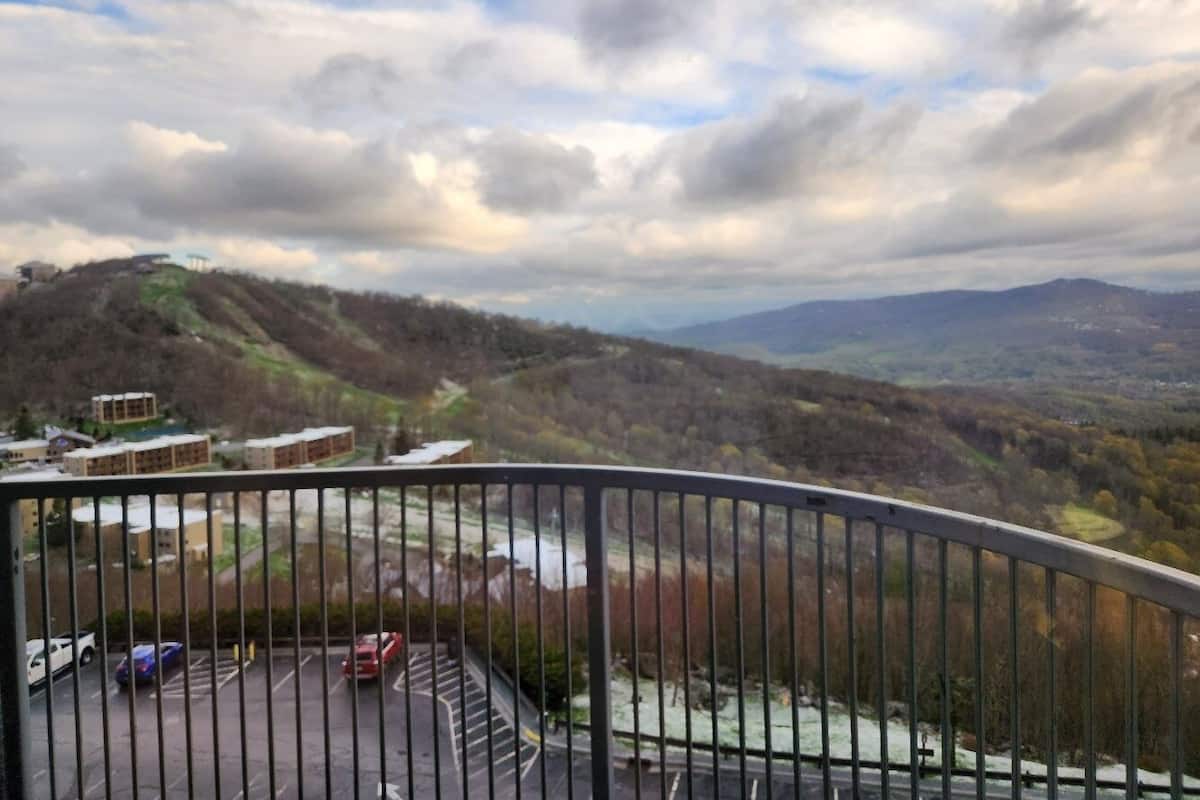 A balcony with a view of a parking area and distant hills.