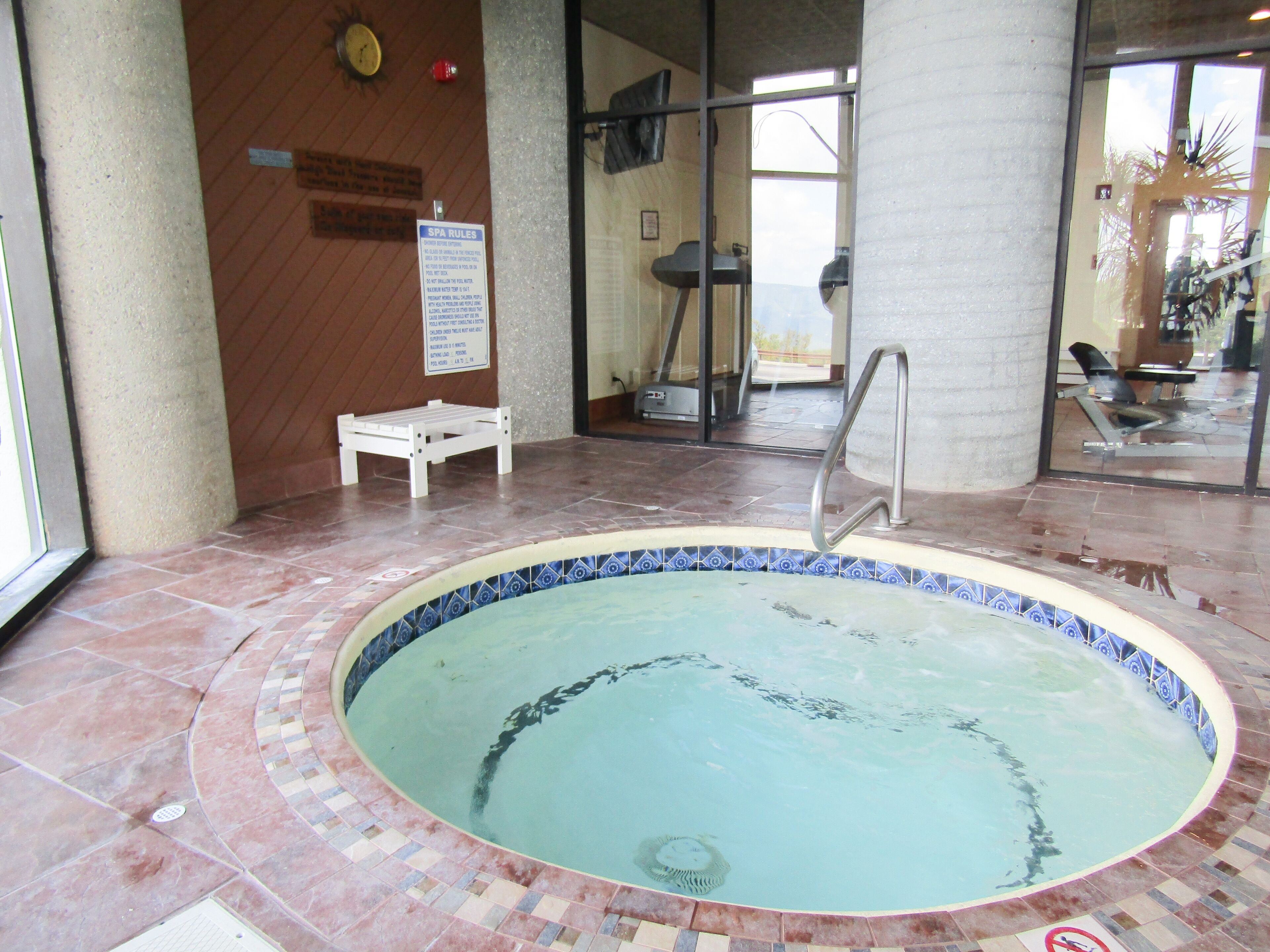 Een wellnessbad met betegelde rand, een bank en een bord met badregels.