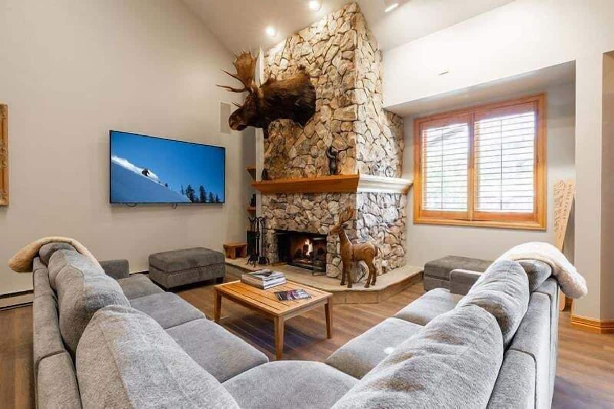 Ein Wohnzimmer mit Kamin aus Stein, einem aufgehängten Elchgeweih und einem Fernseher an der Wand.