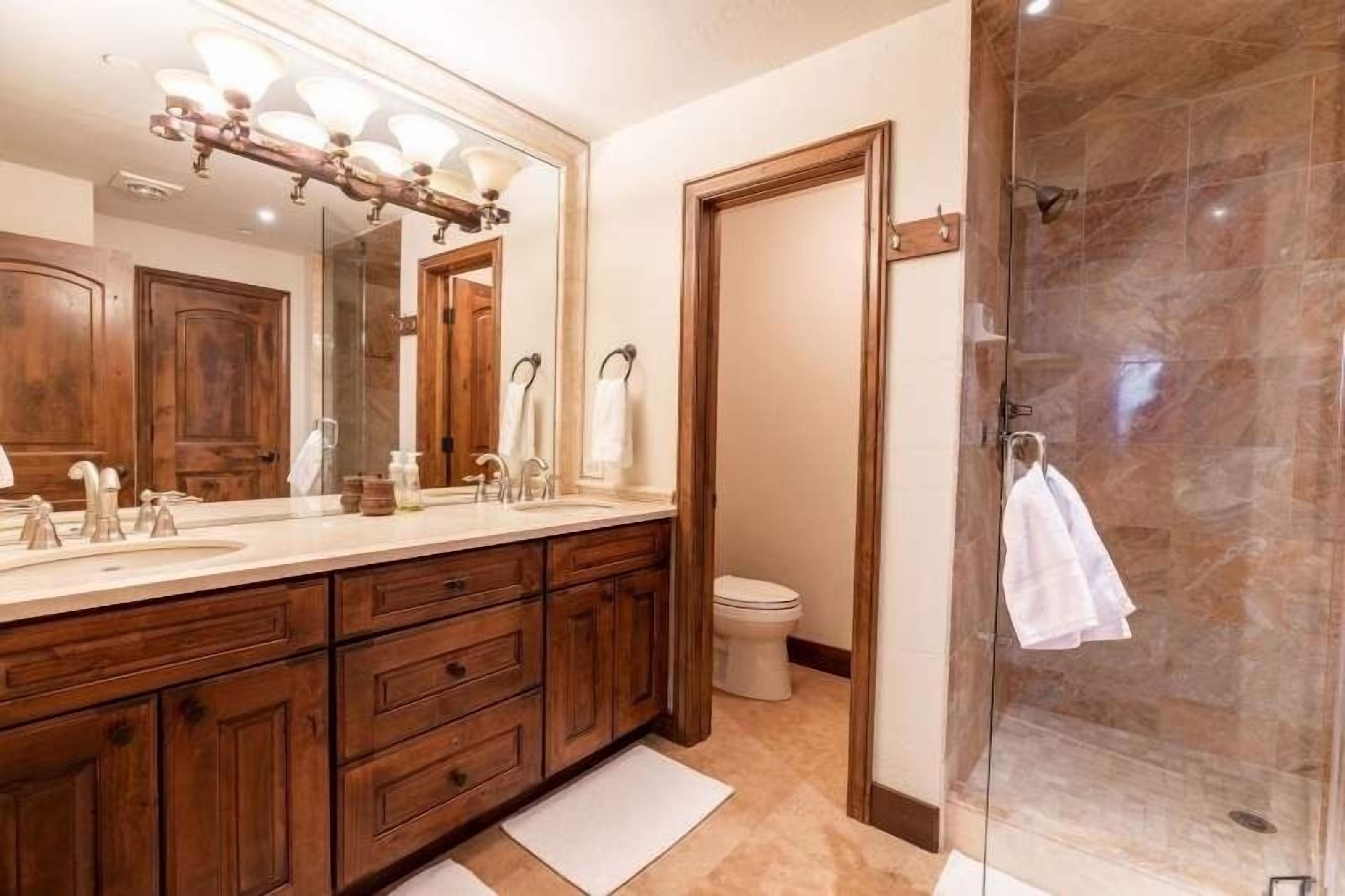 Un baño moderno con un espejo grande, tocador de madera y cabina de ducha de vidrio.