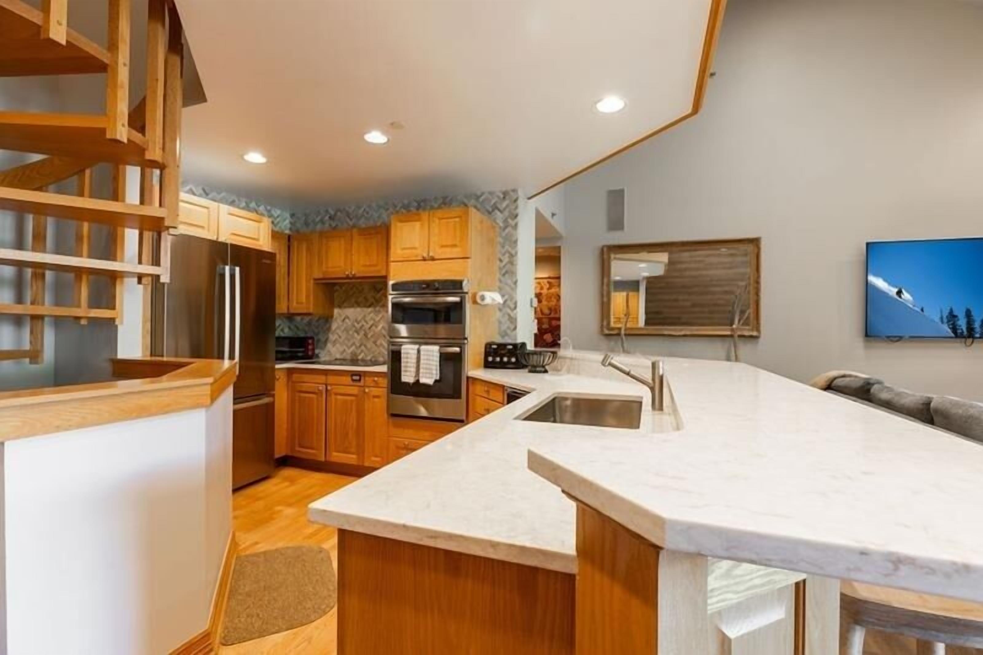 A modern kitchen with wooden cabinets, a marble countertop, and a built-in oven.